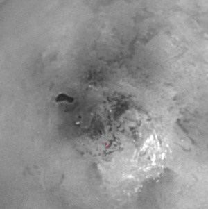Титан. Красным крестиком отмечен южный полюс, яркие белые пятна — метановые облака. Темное пятно может соответствовать озеру с жидким водородом или же останкам такого озера (фото с сайта saturn.jpl.nasa.gov)